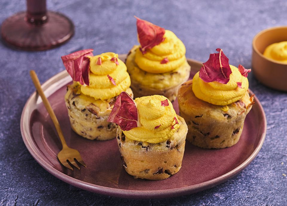 Four savoury muffins with yellow mousse and purple radicchio leaves on a plum-coloured round plate.