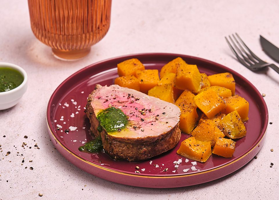 A rare slice of beef with salsa verde and roasted pumpkin cubes, served on a burgundy-coloured plate.