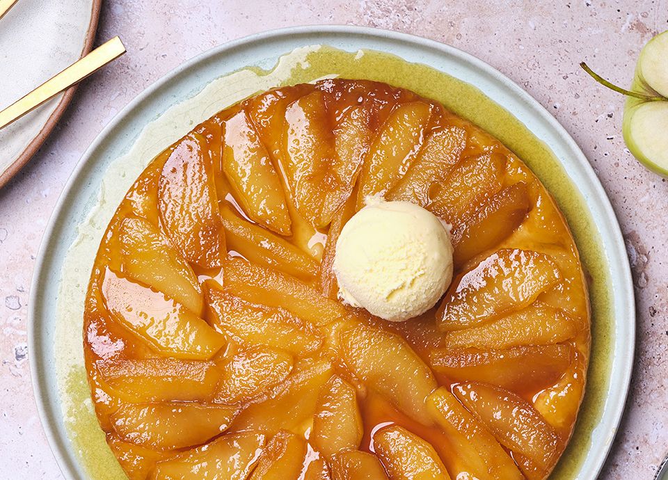 A cake topped with caramelised apples arranged in a radial pattern, with a scoop of ice cream in the centre, served on a light blue plate.