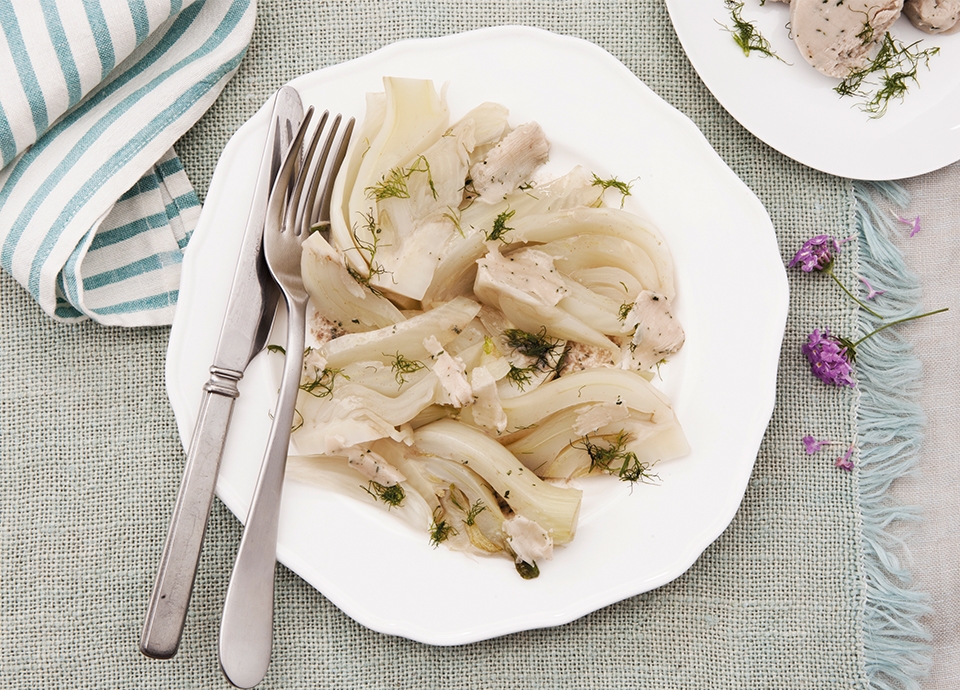 Steamed fennel wedges with anchovy butter and fresh dill on a white plate with silverware and a striped napkin.