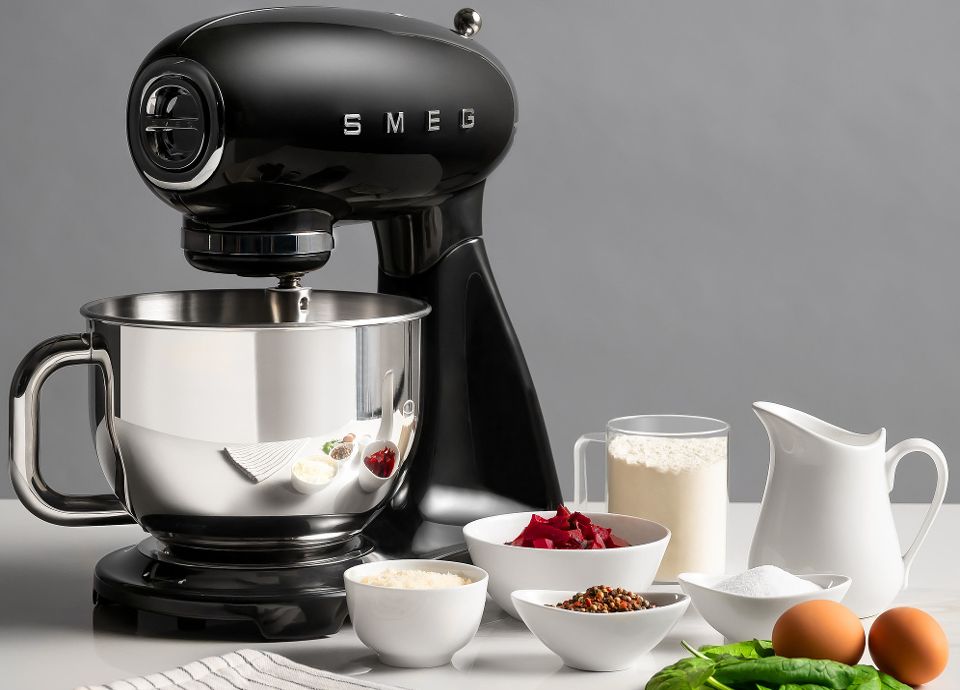 A black Smeg stand mixer on a counter surrounded by bowls of flour, beetroots, spinach, and spices.