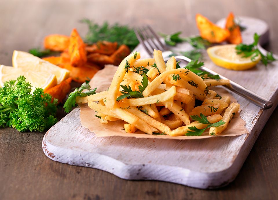 Golden fried potatoes served on a wooden board with fresh herbs and lemon.