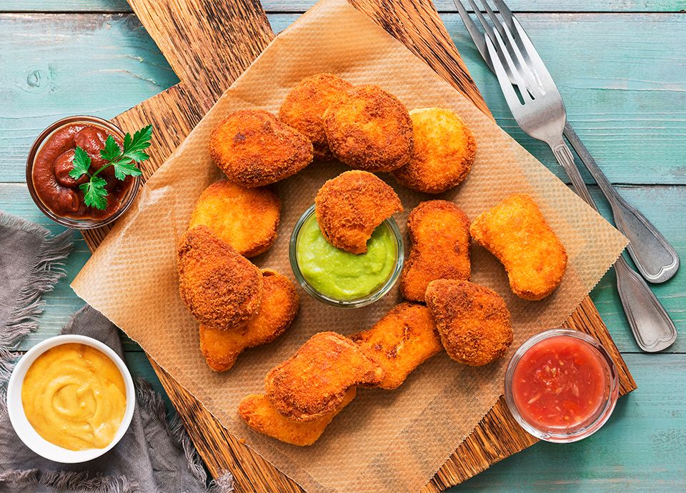 Tray with fried nuggets arranged on parchment paper, accompanied by three sauces in small bowls.
