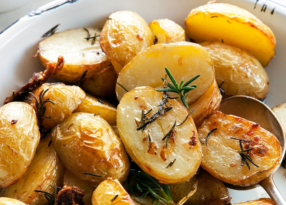 Crispy, halved golden roasted potatoes seasoned with fresh rosemary sprigs in a white serving dish.