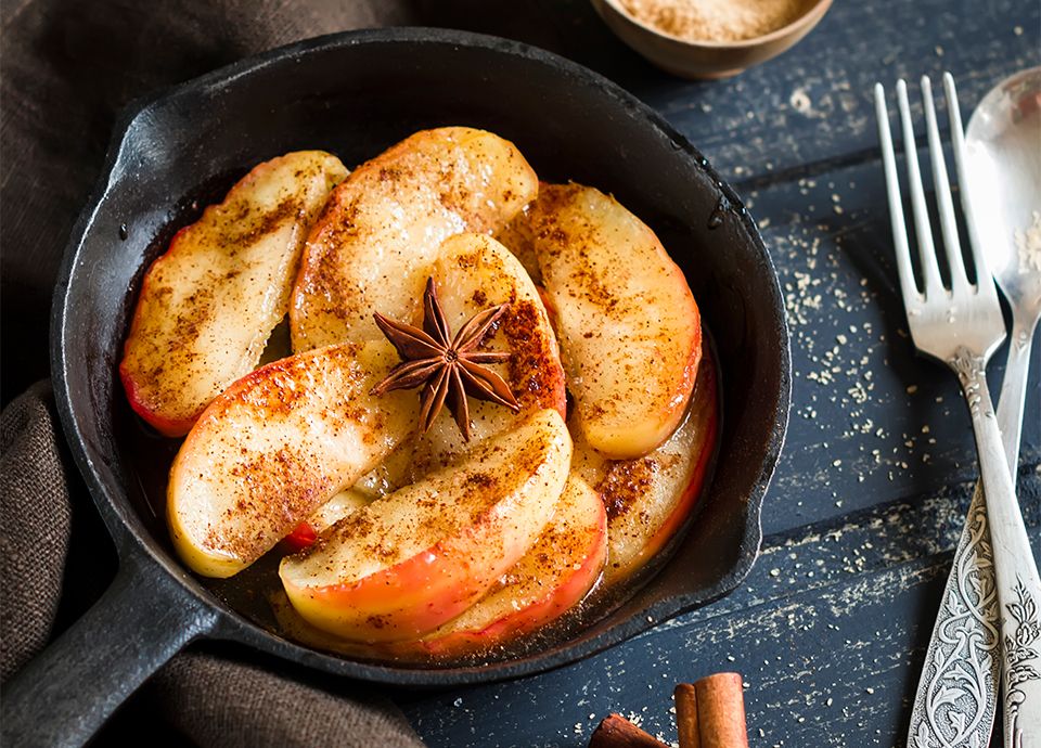 Sliced apples dusted with cinnamon and topped with star anise in a black cast-iron skillet.