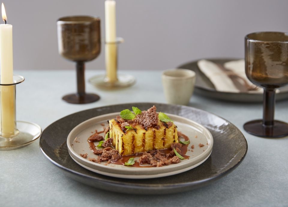 A golden-brown grilled pineapple slice topped with buttery crumble, caramel sauce, and fresh mint on a white plate.
