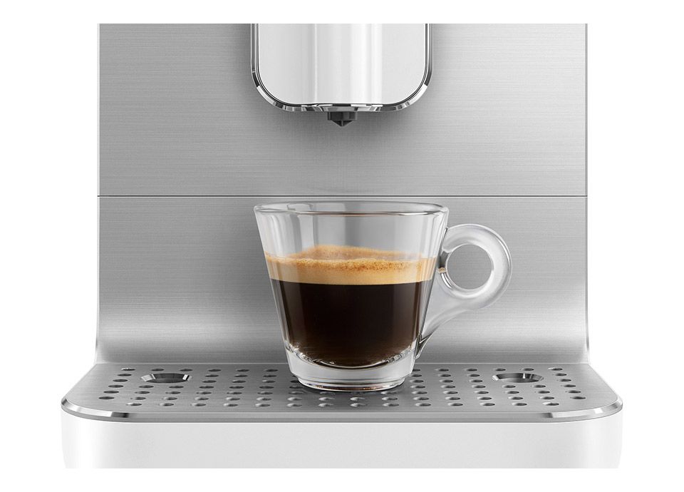 Close-up of a glass cup filled with espresso under a stainless steel Smeg coffee machine on a drip tray