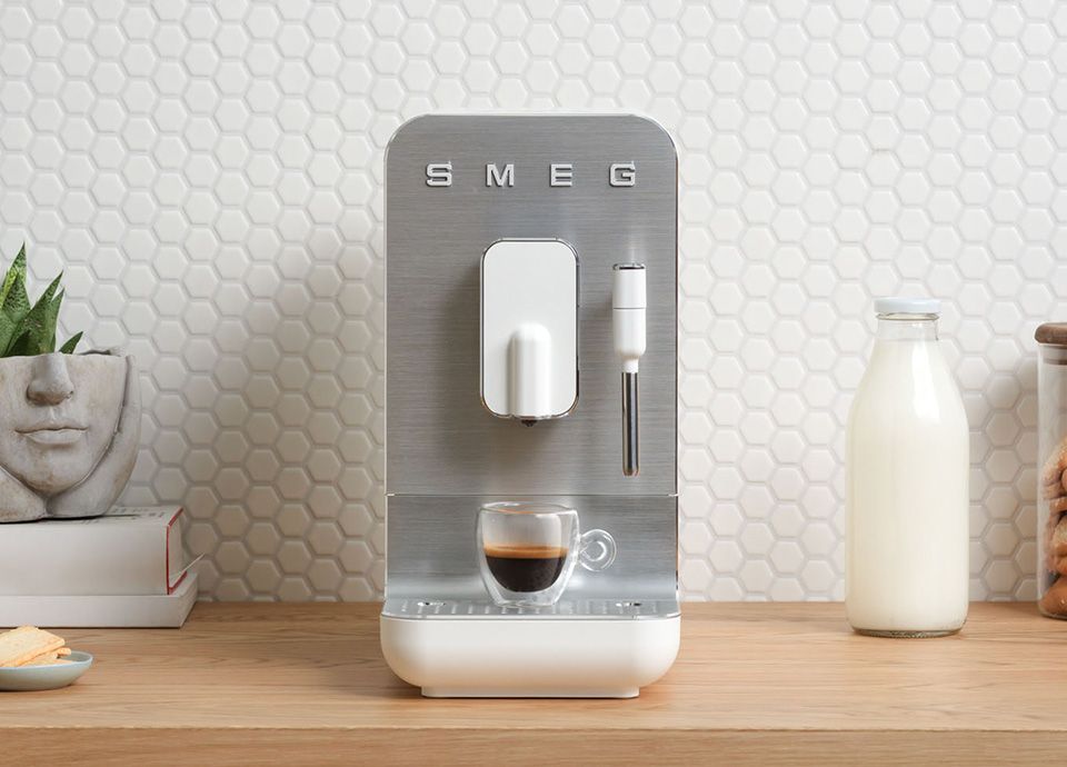 Stainless steel Smeg coffee machine with steam wand preparing an espresso on a wooden countertop with milk bottle and kitchen decor