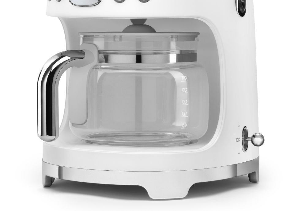 Close-up of the glass carafe with a chrome handle, sitting inside the base of a white matt-finish coffee machine.