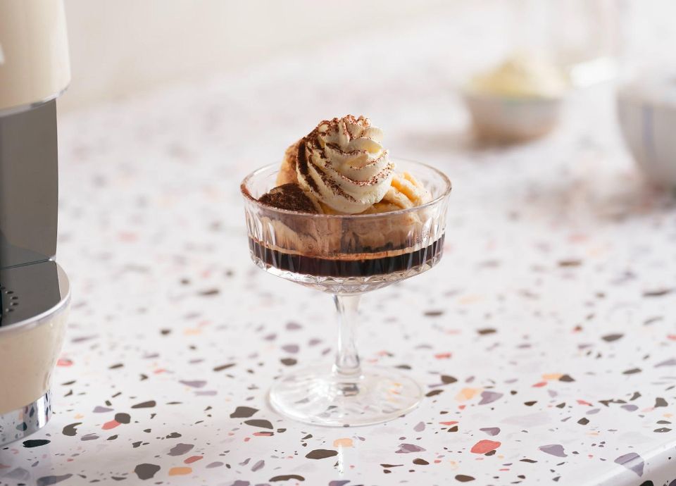 Espresso dessert topped with whipped cream and cocoa powder served in a glass on a terrazzo countertop