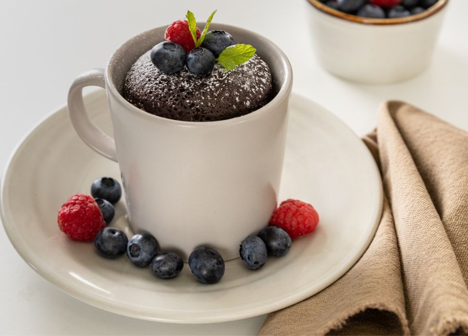 Chocolate mug cake garnished with berries, placed on a white countertop with a beige napkin nearby.