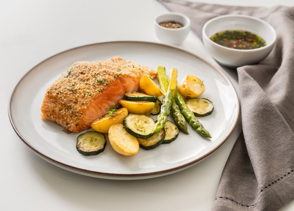 Gratinated salmon fillet served with vegetables on a white ceramic plate.