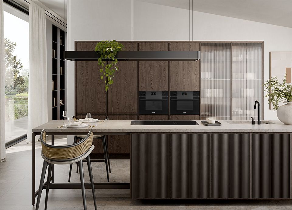 Modern kitchen with dark wood cabinetry, a large island with ribbed panels, integrated appliances, and a minimalist black range hood with hanging greenery.