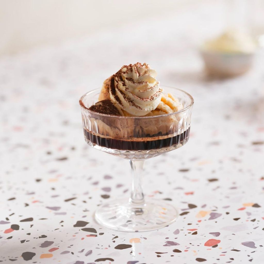 Coffee-flavored ice cream with a scoop of ice cream, whipped cream, and cocoa powder, served in a crystal bowl on a terrazzo-style countertop.