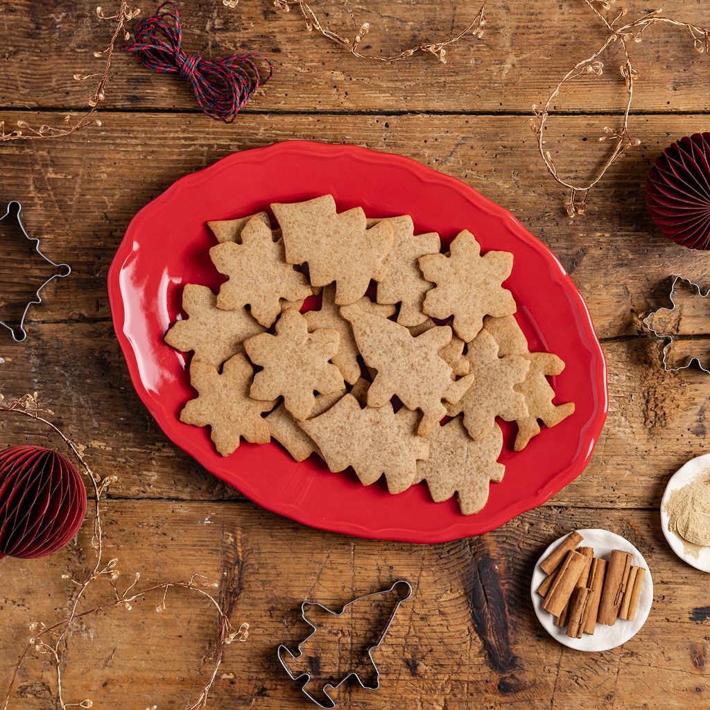 Star- and tree-shaped cookies on a red tray, with cinnamon sticks and cookie cutters on a wooden table.