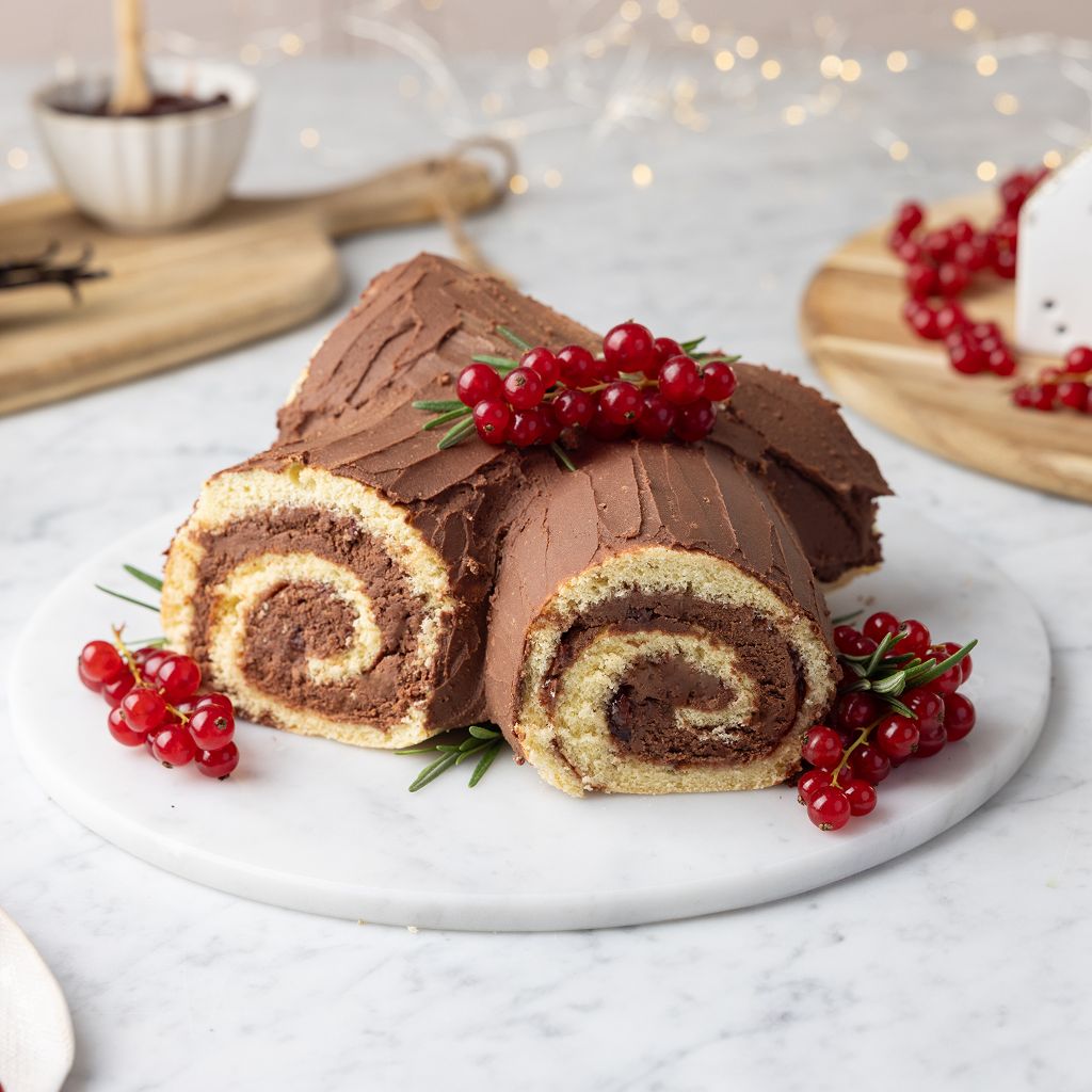 A yule log filled with dark cream, covered in chocolate, and decorated with red currants and sprigs of rosemary.
