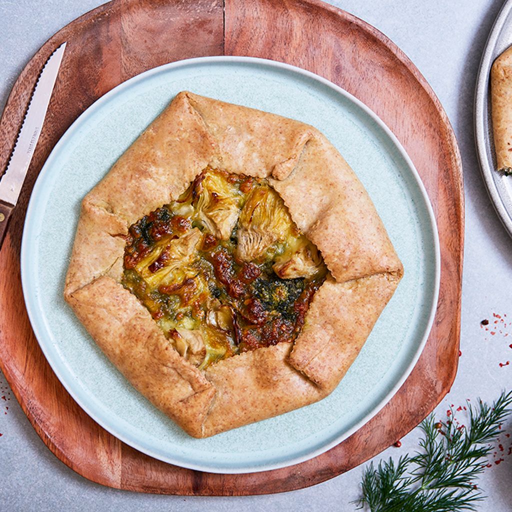 A golden hexagonal cracker filled with artichokes and spinach, served on a blue plate and a circular wooden chopping board.