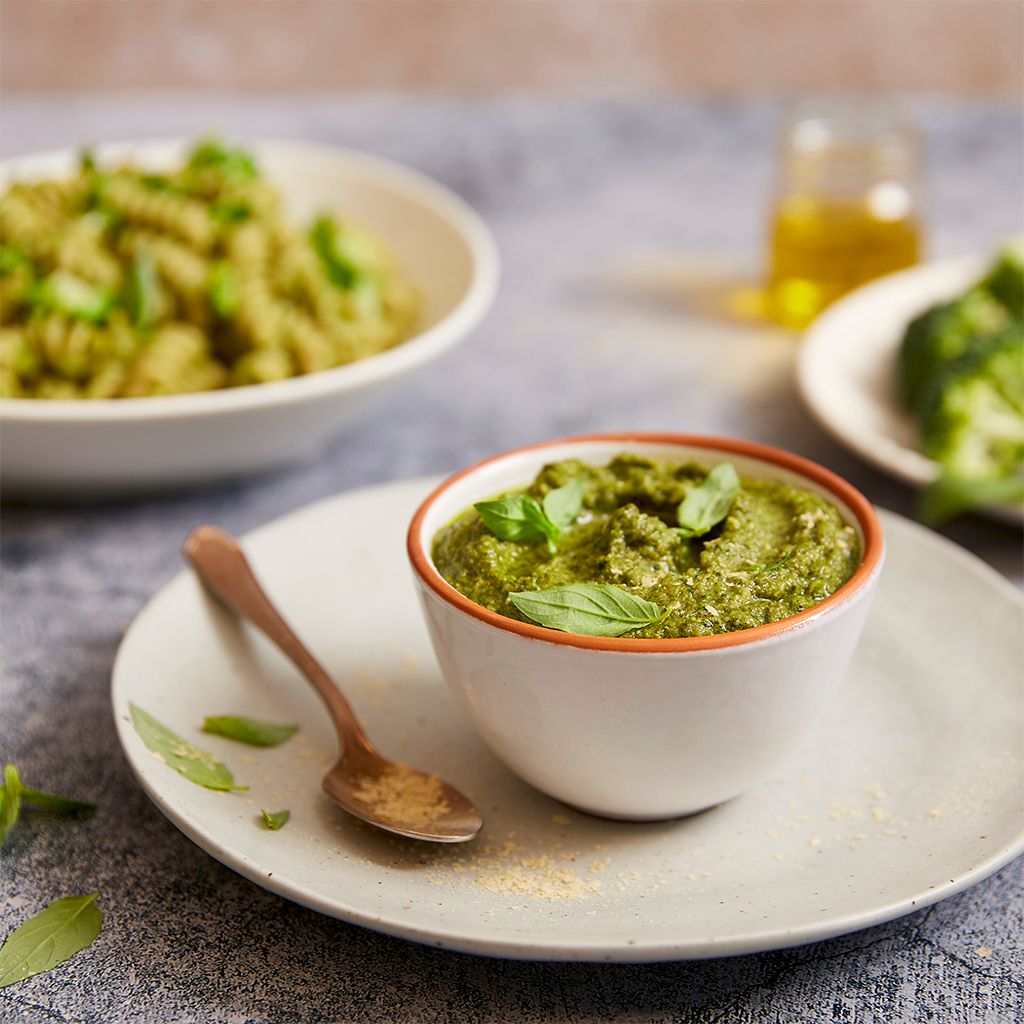 A bowl of green pesto with basil leaves, served with pasta and steamed broccoli.