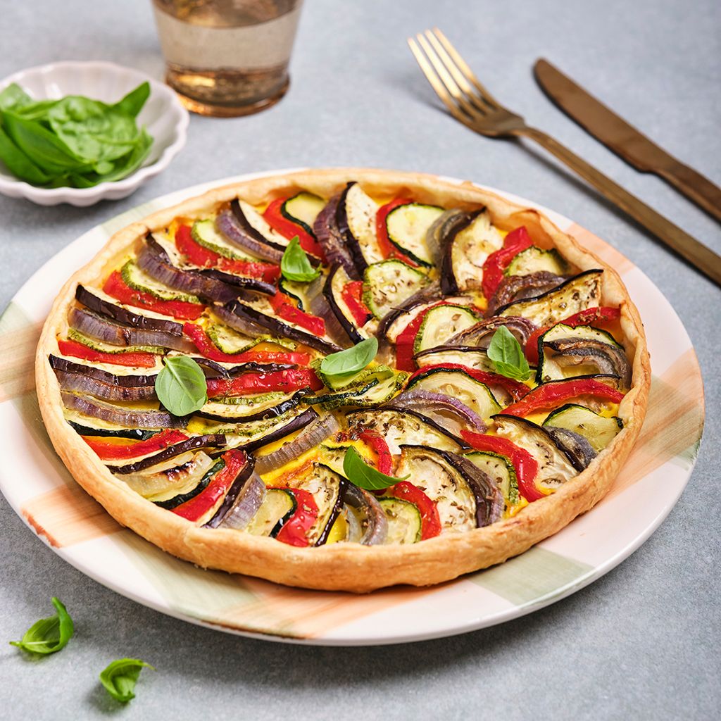 Savory tart with slices of zucchini, eggplant, and bell peppers arranged in a spiral, garnished with basil and oregano.