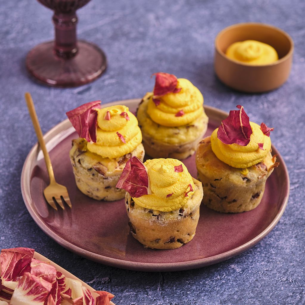 Four savoury muffins with yellow mousse and purple radicchio leaves on a plum-coloured round plate.