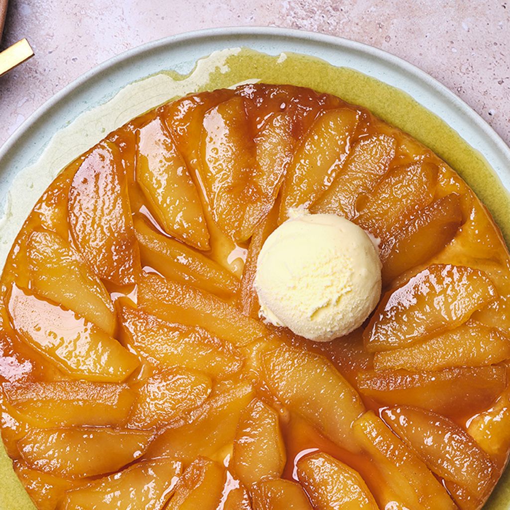 A cake topped with caramelised apples arranged in a radial pattern, with a scoop of ice cream in the centre, served on a light blue plate.
