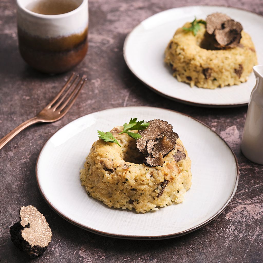 A ring-shaped rice cake garnished with shavings of black truffle and parsley, served on a white dinner plate.