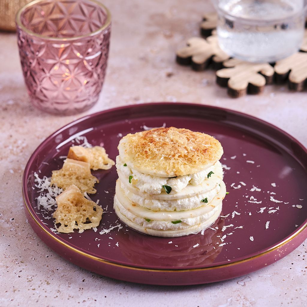 A tower of celeriac and ricotta slices on a burgundy plate, garnished with Parmesan crisps and grated cheese.