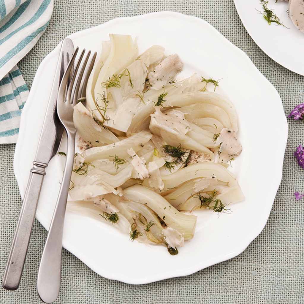 Steamed fennel wedges with anchovy butter and fresh dill on a white plate with silverware and a striped napkin.