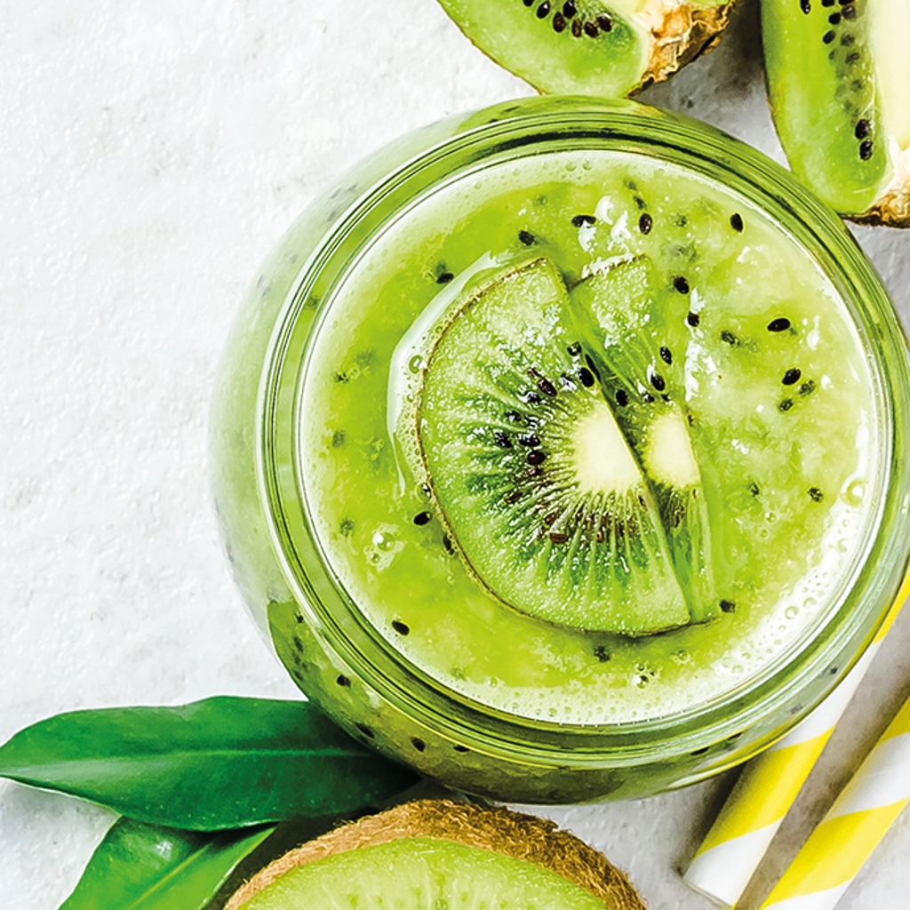 A jar containing green grenadine and slices of kiwi, viewed from above against a white background with yellow and white straws.