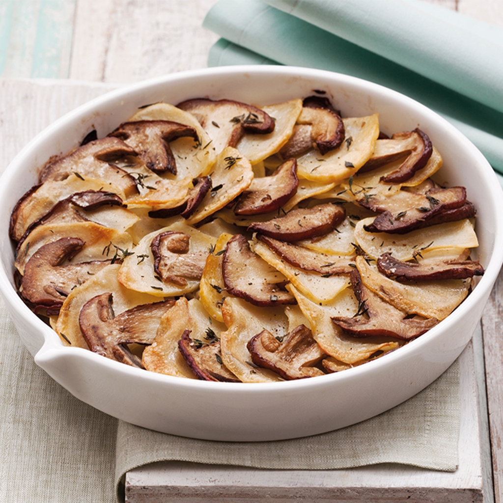 A casserole in a white oven dish with alternating layers of potatoes and slices of golden-brown porcini mushrooms, garnished with thyme leaves.