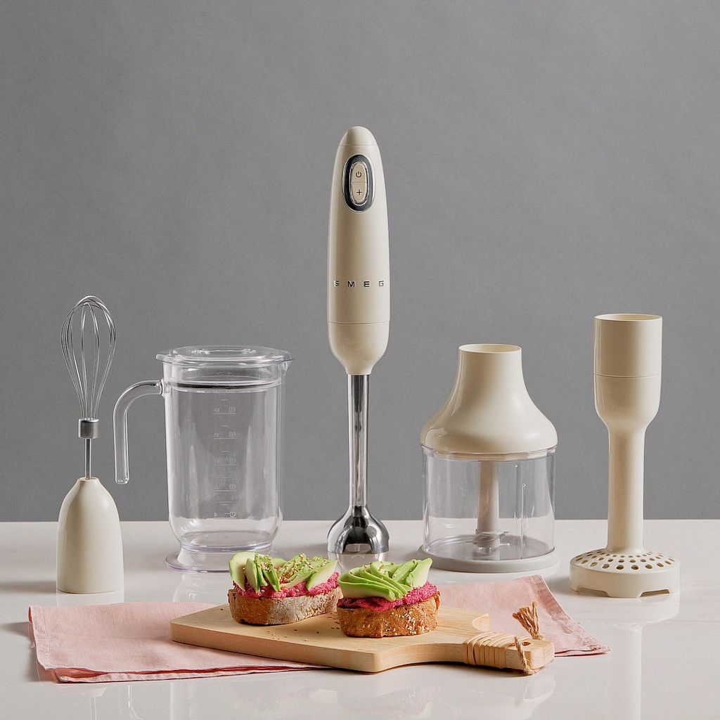 Cream Smeg hand blender and attachments displayed with avocado and beet hummus toast on a wooden board.