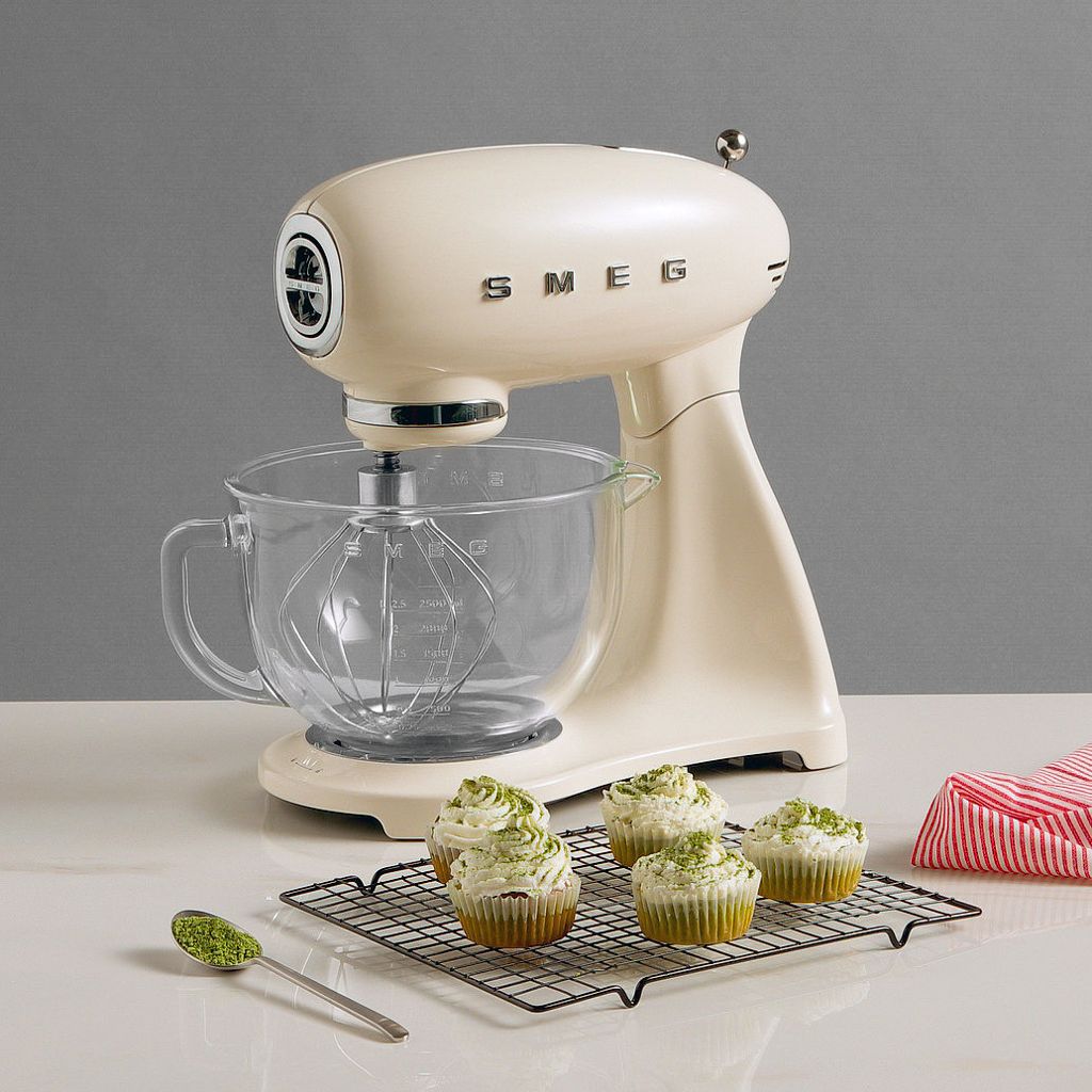 Green matcha cupcakes on a cooling rack next to a cream Smeg stand mixer with a glass bowl.