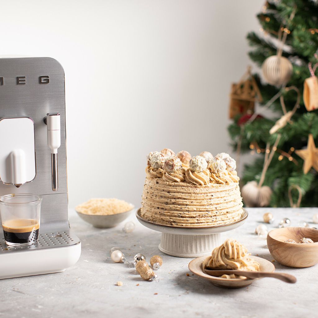 A tall coffee chiffon cake with ribbed frosting and truffle toppings, set against a holiday background with a Smeg machine.