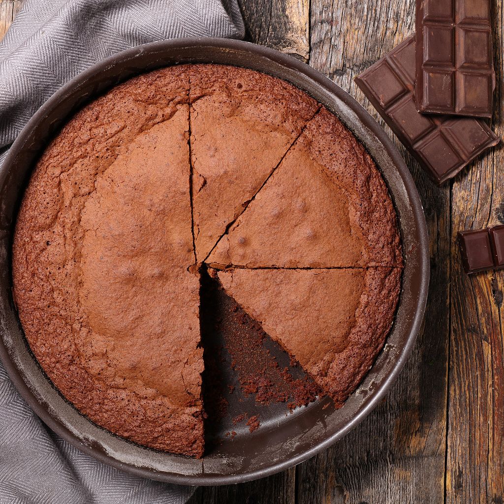 Overhead view of a sliced chocolate caprese cake in a round baking pan, showcasing a rich, moist texture.