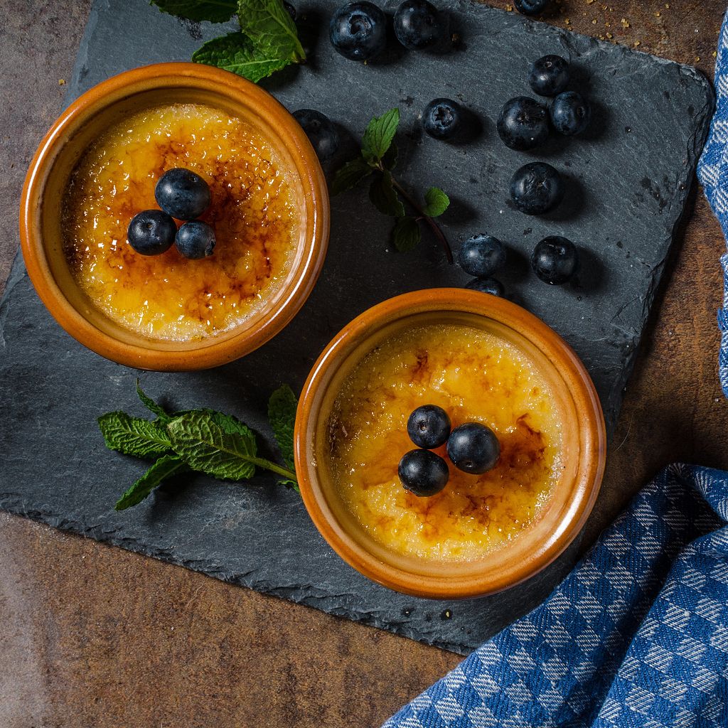 Close-up of a crème brûlée in a white ramekin with a crisp, golden-brown caramelized sugar topping.