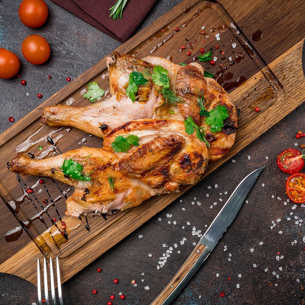Grilled spicy chicken pieces on a wooden board, garnished with fresh cilantro, peppercorns, and a balsamic glaze.