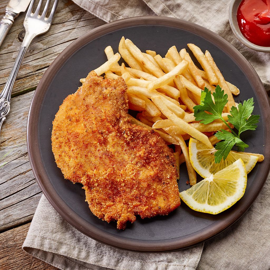 Golden-brown breaded chicken cutlet served with a side of french fries, lemon wedges, and a sprig of fresh parsley.