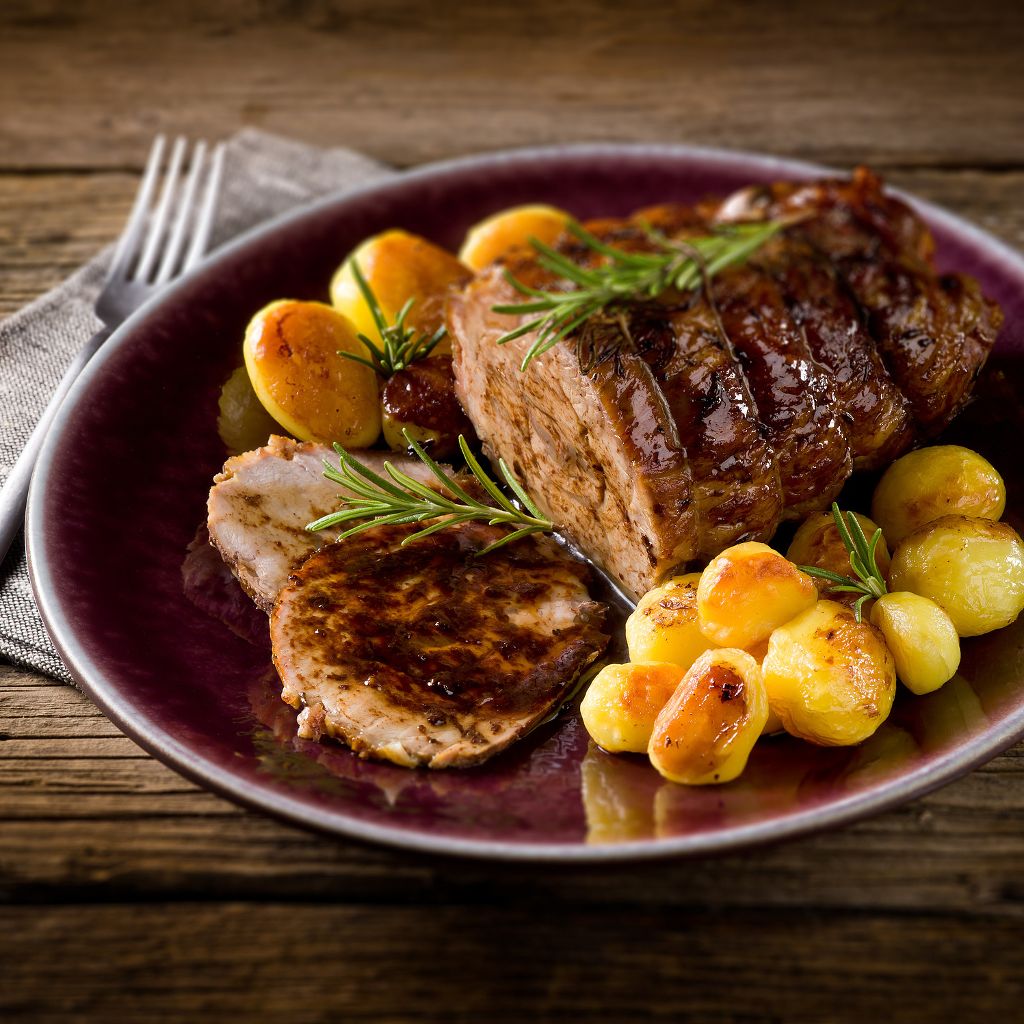 Sliced roast veal served on a dark plate with roasted golden potatoes and a garnish of fresh herbs.
