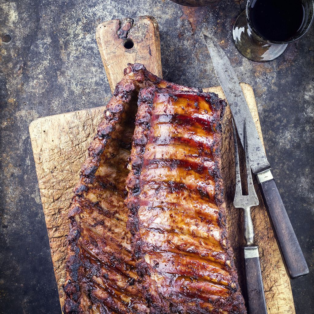 A full rack of glazed, grilled beef ribs served on a wooden cutting board with a knife resting nearby.