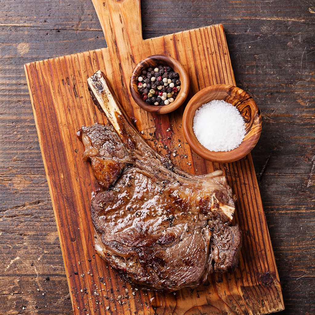 Raw entrecote steak on a wooden cutting board with a small bowl of salt and peppercorns.