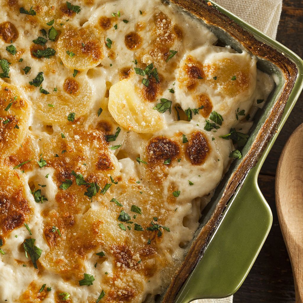 Close-up of sliced potatoes in a creamy white sauce, baked golden-brown and topped with fresh green herbs.
