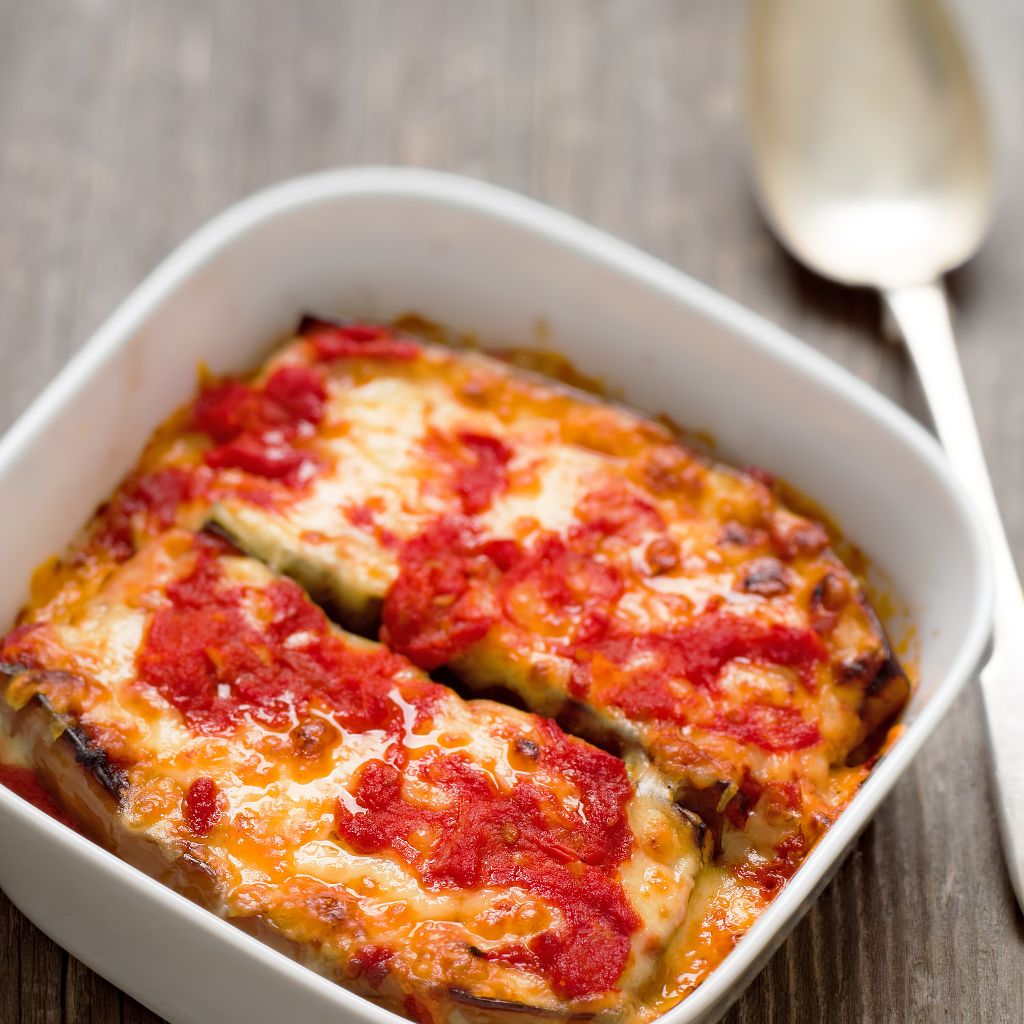 Two thick slices of baked eggplant topped with melted cheese and red tomato sauce in a white ceramic baking dish.