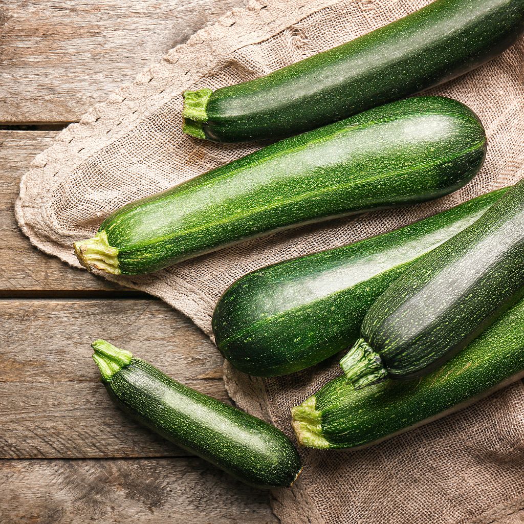 Close-up of several whole dark green zucchini on a tan burlap cloth and rustic wooden surface.