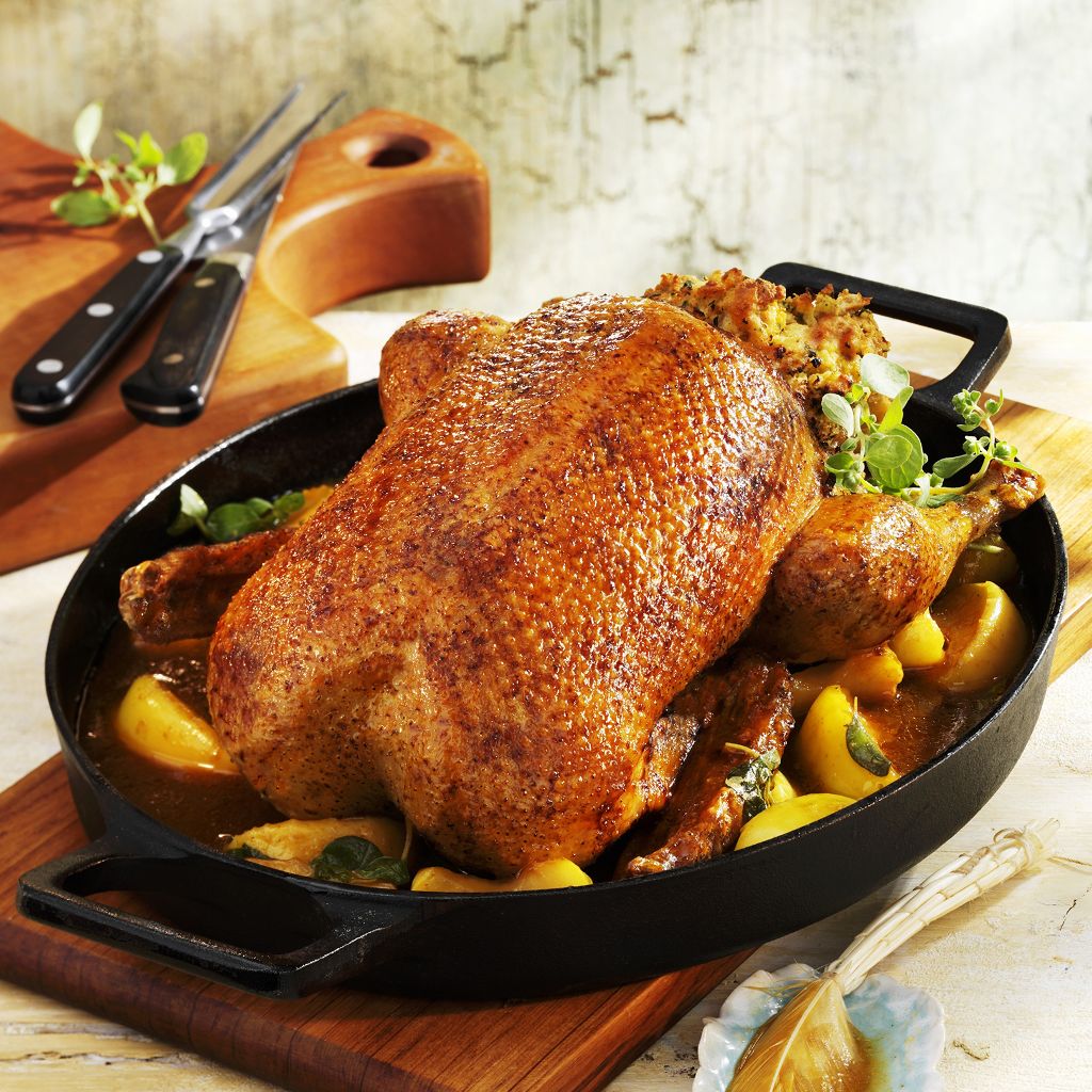 A whole golden-roasted guinea fowl in a cast iron pan, surrounded by roasted fruit and topped with herb stuffing.