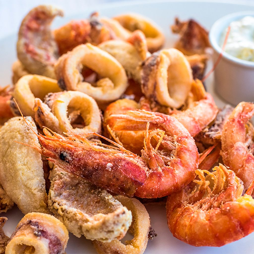 Mixed fried calamari and shrimp served with a lemon wedge and a dipping sauce in a small bowl.