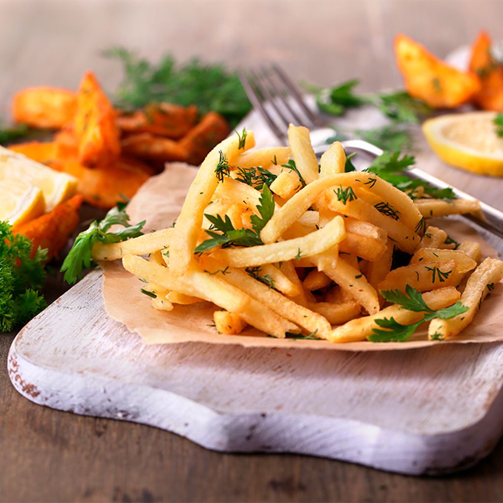 Golden fried potatoes served on a wooden board with fresh herbs and lemon.