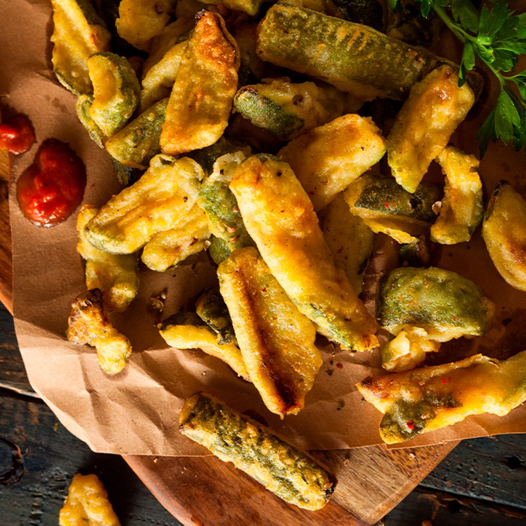 Battered vegetables served on kitchen paper, accompanied by a red sauce and a sprig of parsley.