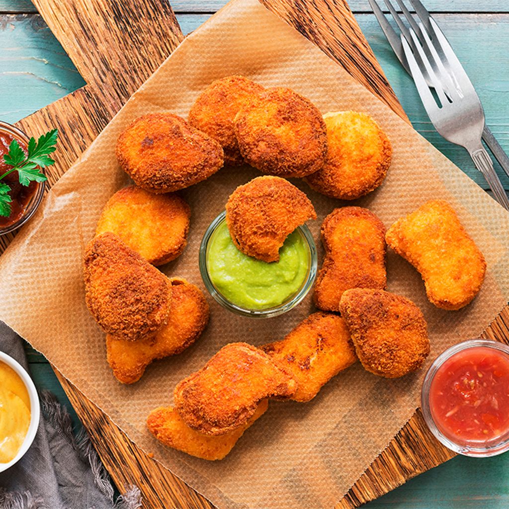 Tray with fried nuggets arranged on parchment paper, accompanied by three sauces in small bowls.