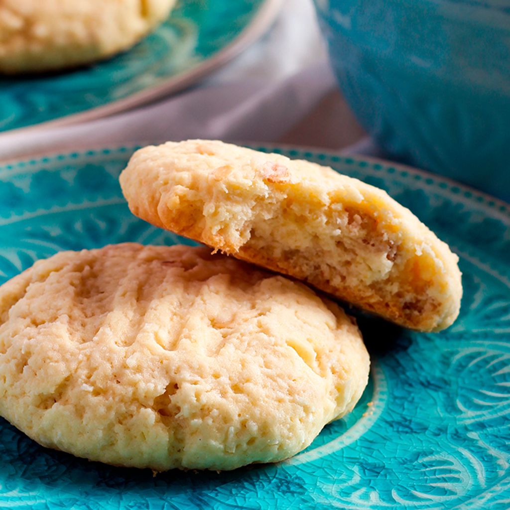 Two golden corn biscuits on a teal patterned plate, one broken in half to show the soft, crumbly interior.