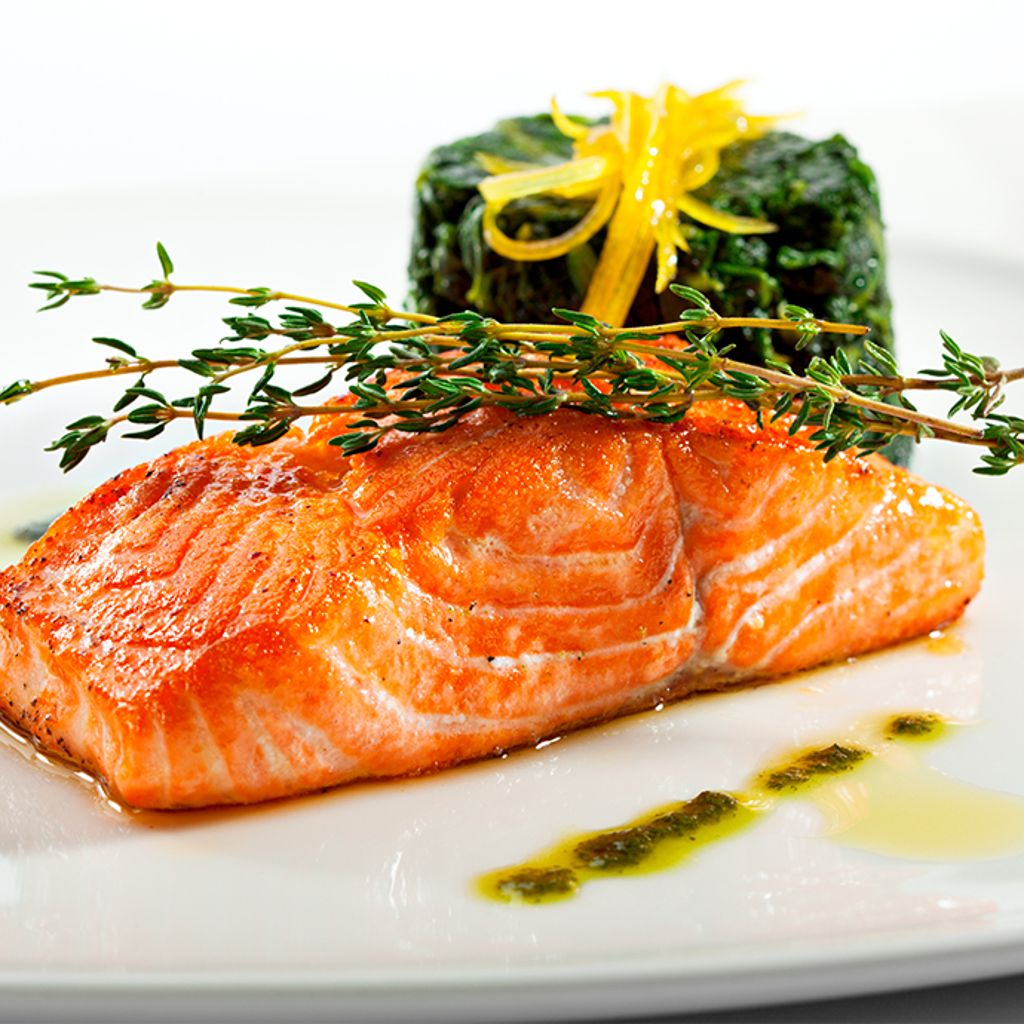 A seared salmon fillet garnished with thyme sprigs, served with a side of greens and lemon zest on a white plate.